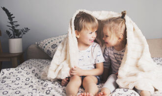 Two Pretty Kids Embrace Under Blanket